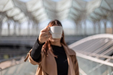 Mulher segurando uma chávena de café em um ambiente moderno, destacando a combinação de creatina e cafeína juntas.