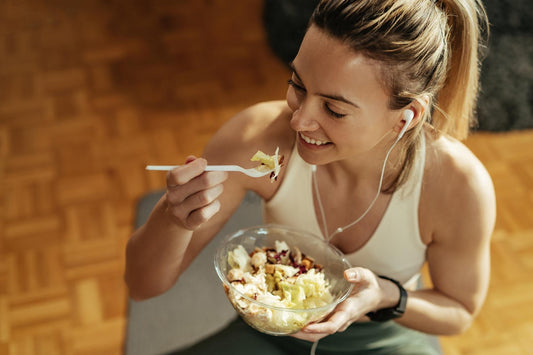 Mulher sorrindo enquanto come salada, enfatizando a importância de alimentos ricos em probióticos na dieta.